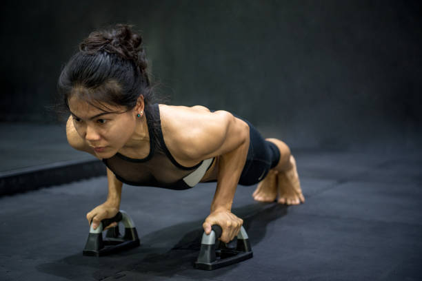 Young Asian athlete woman doing push up with push-up bars on the floor stock photo