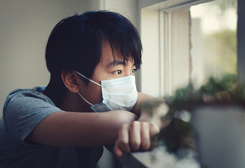 Young Asian boy in home quarantine, sitting near a window