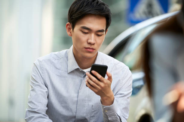 young asian business person using cellphone while waiting in line stock photo