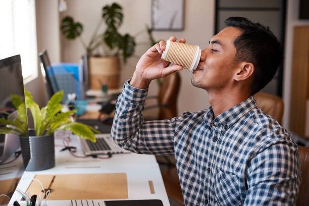 A young Asian businessman drinks coffee at his desk in an empty office stock photo