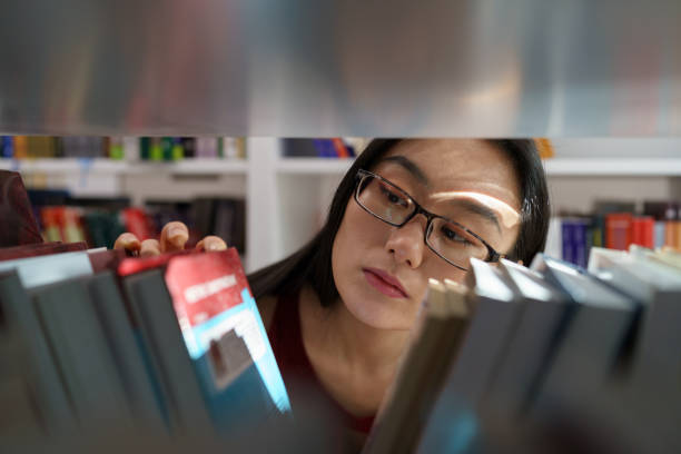 Young asian college girl searching for academic journals, books and primary sources in library stock photo