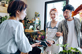 istock Young Asian couple buying flowers in flower shop. Boyfriend is paying for the bouquet with his smartphone, scan and pay a bill on a card machine making a quick and easy contactless payment. NFC technology, tap and go concept 1366715833