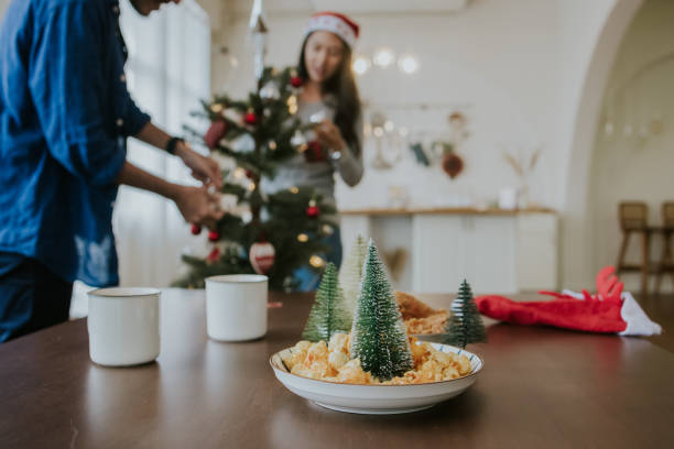 Young Asian couple decor Christmas tree and preparing some food together at home - stock photo stock photo