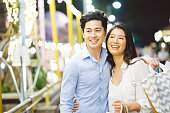 Young asian couple enjoying shopping in the night market, they are walking around, taking and smiling