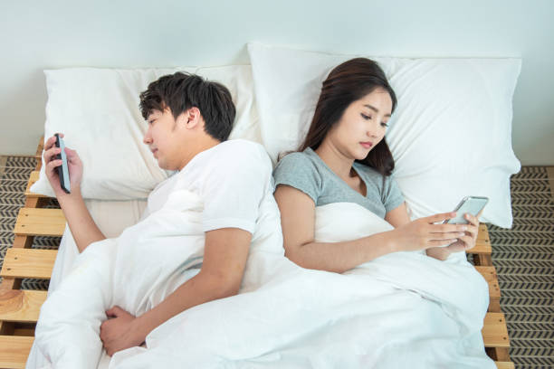 cặp vợ chồng trẻ châu á trên giường sử dụng điện thoại nằm ngửa với nhau. người đàn ông và phụ nữ châu á sử dụng điện thoại di động thông minh riêng với sự riêng tư, vấn đề mối quan hệ  - chia ly hình ảnh sẵn có, bức ảnh & hình ảnh trả phí bản quyền một lần