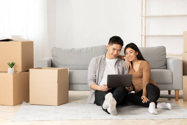 Young asian couple using laptop sitting on floor Online Ordering Concept. Asian family using laptop sitting on floor among boxes, empty space filipino family stock pictures, royalty-free photos & images