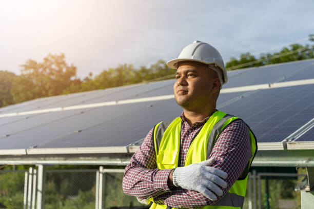 Young asian electrical engineer standing in front of Solar cell panels farm. He checking and installing. Solar generator power concept. stock photo