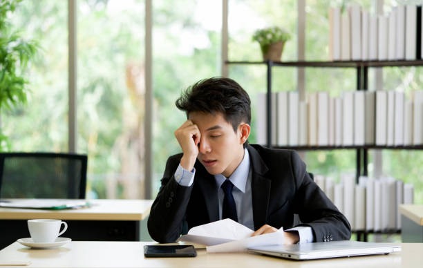 Young asian employee take a nap in the office on a table with tablet and laptop computer. stock photo