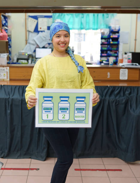 A young asian female frontliner holding a sign showing that she had taken her booster dose of Covid-19 vaccine at a local healthcare facility. stock photo