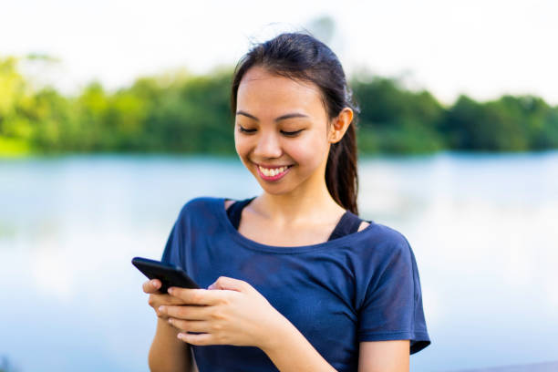 Young Asian fitness woman using mobile phone by a lake Young Asian fitness woman using mobile phone by a lake filipino woman stock pictures, royalty-free photos & images