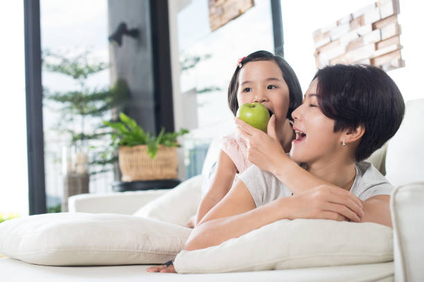 Young Asian girl eating apple with her mother at home. stock photo