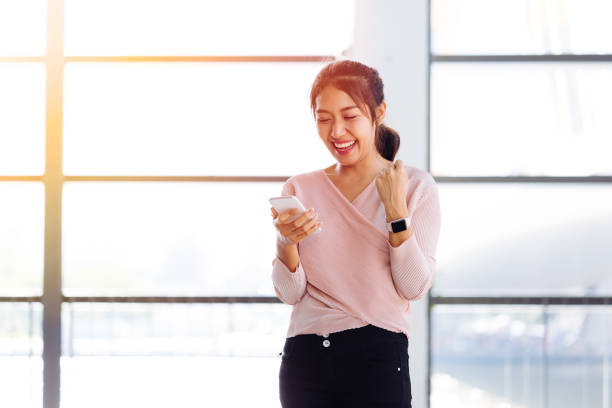 Young Asian girl looking at her mobile phone and get excited inside the building Young Asian girl looking at her mobile phone and get excited inside the building. One beautiful woman is happy watching at smartphone indoors. indonesian girl stock pictures, royalty-free photos & images