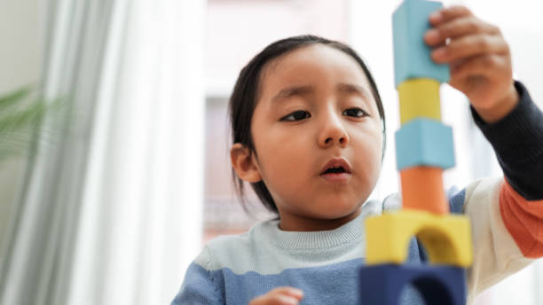Young asian kid playing with color blocks at home - Kindergarten educational games - Focus on boy mouth stock photo