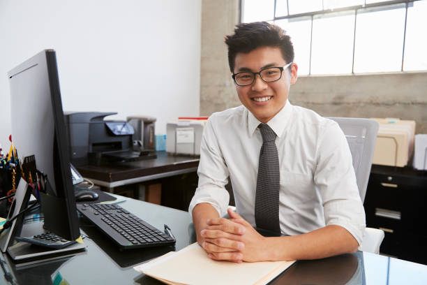ung asiatisk manlig professionell vid skrivbord leende till kamera - man jobbar dator ögonkontakt bildbanksfoton och bilder