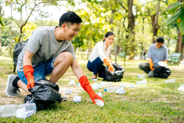 Young Asian man and women wearing orange gloves and collecting trash in garbage bag in the park Young Asian man and women wearing orange gloves and collecting trash in garbage bag in the park. Save the earth and environmental concern concept garbage photos stock pictures, royalty-free photos & images