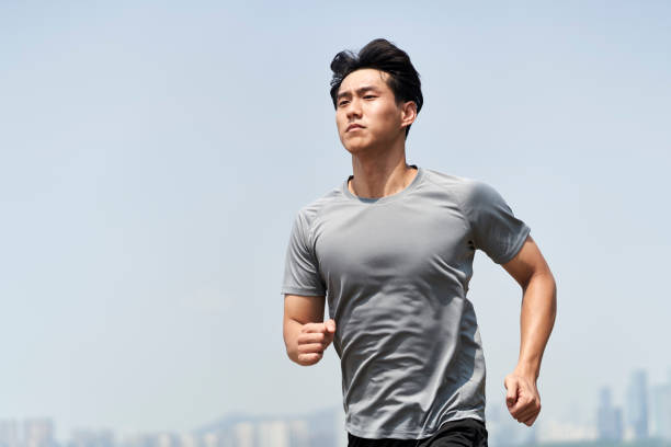 young asian man athlete running on beach stock photo