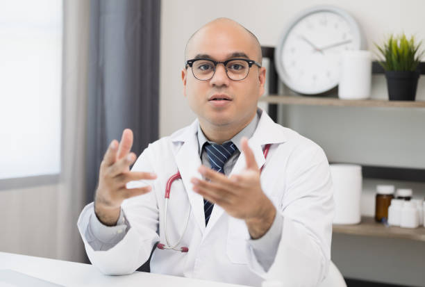 Young asian man doctor works from home working online looking and camera talking with patient Explain about taking medications to treat illnesses. stock photo