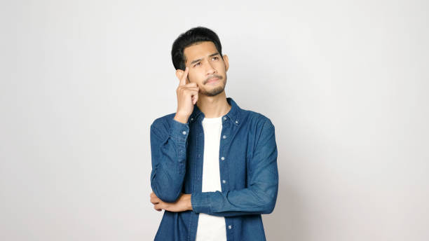 Young asian man serious thinking while standing over isolated grey background, Portrait of asia guy showing face expression stock photo