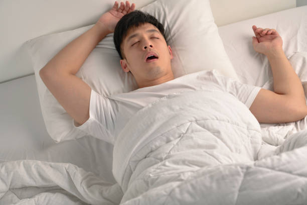Young Asian man sleeping and snoring loudly lying in the bed stock photo