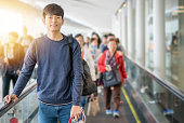 若いアジア人は公共交通機関で旅行し、空港で電車を待っています