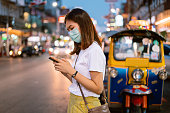 Young asian solo travel use moblie phone call taxi / bus transportation at chinatown road Bangkok thailand ,wearing facemask  Covid-19 or coronavirus ,travelin new normal concept
