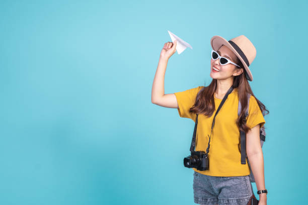 Young Asian woman backpacker traveler holding paper plane over blue background for travel concept Young Asian woman backpacker traveler holding paper plane over blue background for travel concept free cam to cam stock pictures, royalty-free photos & images