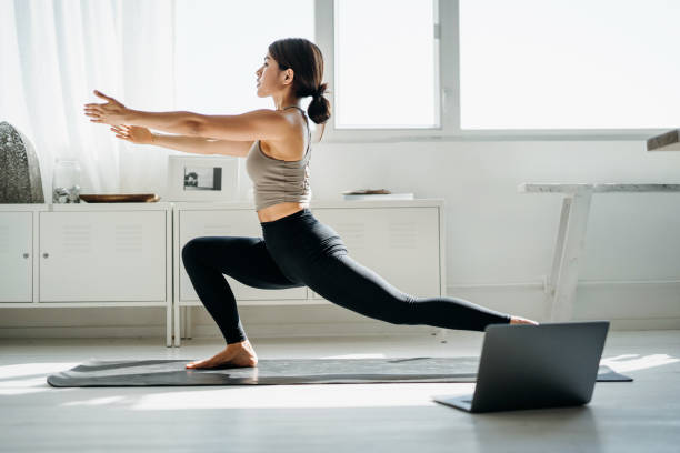 朝、自宅のリビングルームでラップトップでオンラインヨガのクラスをしている若いアジアの女性 - yoga ストックフォトと画像