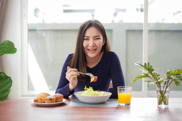 Young asian woman eating healthy salad with fresh vegetable and dip tomato with a fork stock photo