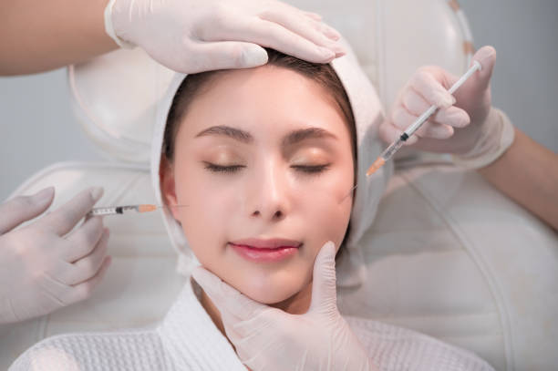 Young Asian woman getting cosmetology treatment facial skin injection by doctor beautician in beauty clinic. stock photo