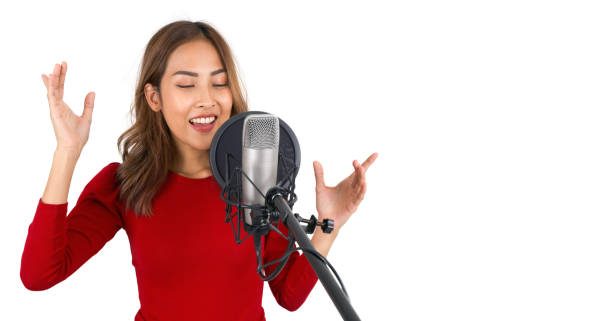 Young asian woman in red t-shirt singing with microphone on white background. Musician producing music in professional recording studio. stock photo