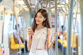 Young Asian woman passenger listening music via smart mobile phone in subway train when traveling in big city