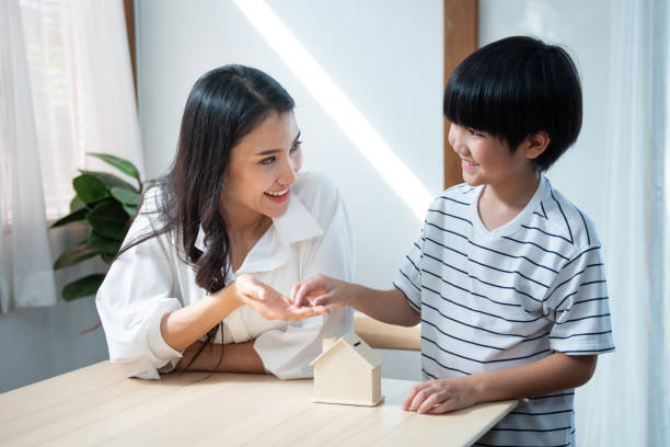 Young asian woman teach her son save money have good financial. cute asian son hand coin on mother hand with house form saving box with smile,Young asian woman teach her son save money have good financial. asian mother talking with daughter stock pictures, royalty-free photos & images