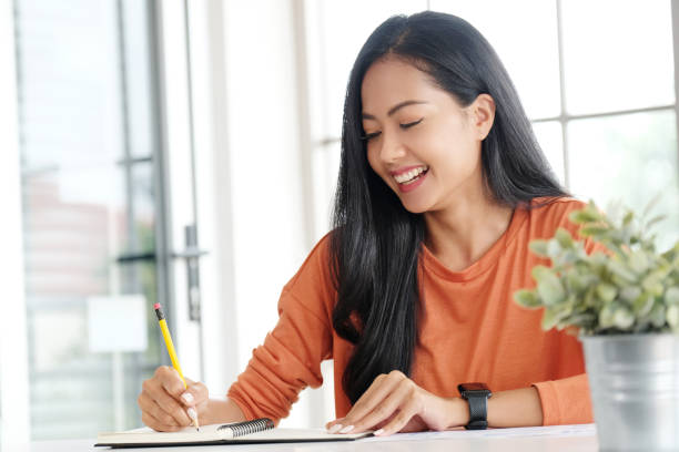 Young asian woman wrting on notebook paper on table at home office stock photo