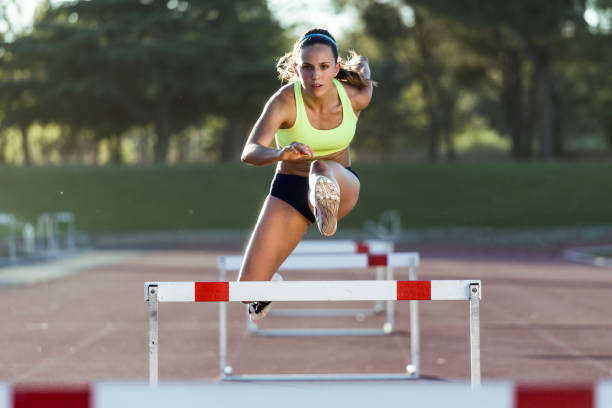 Young athlete jumping over a hurdle during training on race track. stock photo