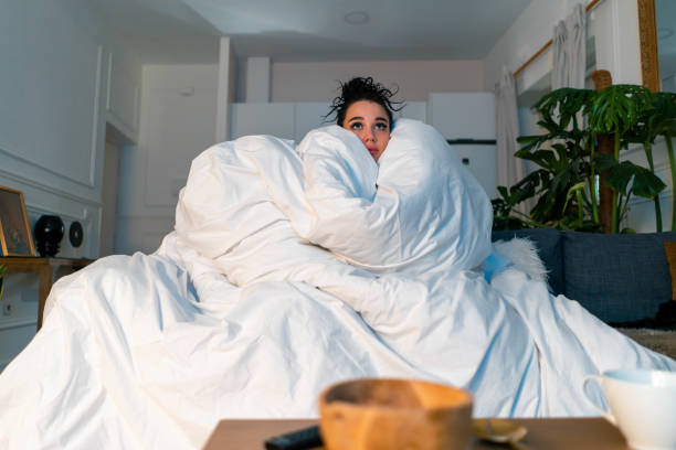 jonge aantrekkelijke angstige vrouw kijken tv-serie en wrapping in grote witte deken. koude herfst-of wintertijd-uitgaven - koud stockfoto's en -beelden