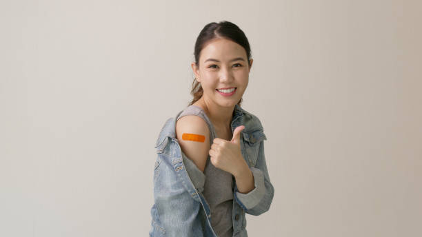 Young attractive beautiful asia female or teenage receive covid-19 anti virus vaccine in campaign vaccination safe life happy smile cheerful with blue, yellow, pink bandage on arm with copy space. stock photo