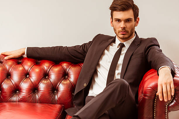 Young attractive businessman Modern young handsome businessman dressed in classical suit posing while sitting on a sofa in the suit shop mens fashion stock pictures, royalty-free photos & images