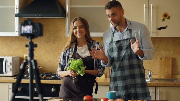 Young attractive couple shooting video food blog about cooking on dslr camera in the kitchen stock photo
