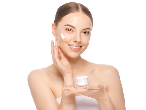 Young attractive woman applying face cream from jar after shower, standing with naked shoulders, isolated on white background Young attractive woman applying face cream from jar after shower, standing with naked shoulders, isolated on white background applying face cream stock pictures, royalty-free photos & images