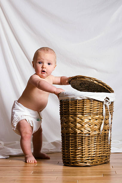 Young baby in reusable nappies looking in laundry basket stock photo