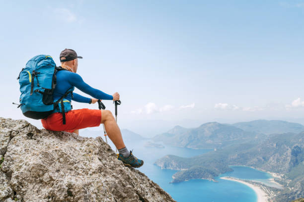Young backpacker man sitting on cliff and enjoying the Mediterranean Sea bay at Oludeniz during Lycian Way trekking walk. Famous Likya Yolu Turkish route. Active sporty people vacations concept image stock photo
