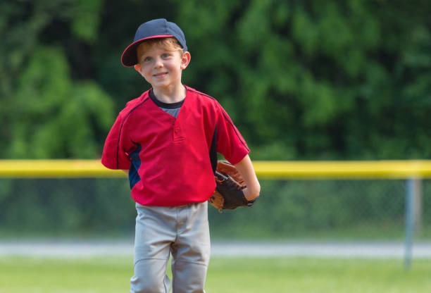 A Young Baseball Player Enjoying the Game A little boy smiles as he plays the field during a baseball game. baseball uniform stock pictures, royalty-free photos & images