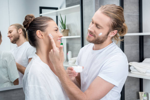 Young bearded husband applying face cream on cheek of his wife  in bathroom Young bearded husband applying face cream on cheek of his wife  in bathroom applying face cream stock pictures, royalty-free photos & images