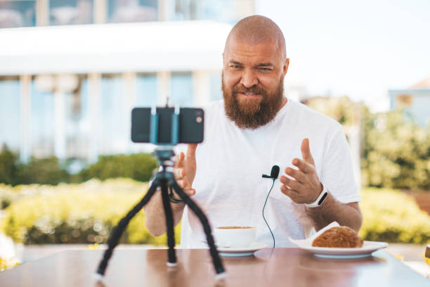 Young bearded man speaks in front of camera - blogging (vlogging) and technology concept stock photo