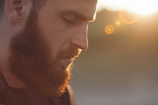 young bearded man with closed eyes on the background of the sun's rays