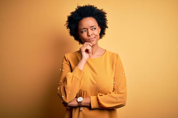 Young beautiful African American afro woman with curly hair wearing casual t-shirt with hand on chin thinking about question, pensive expression. Smiling with thoughtful face. Doubt concept. Young beautiful African American afro woman with curly hair wearing casual t-shirt with hand on chin thinking about question, pensive expression. Smiling with thoughtful face. Doubt concept. confusion stock pictures, royalty-free photos & images