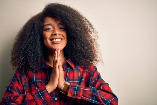 Young beautiful african american woman wearing casual shirt over isolated background praying with hands together asking for forgiveness smiling confident.  prayer request stock pictures, royalty-free photos & images
