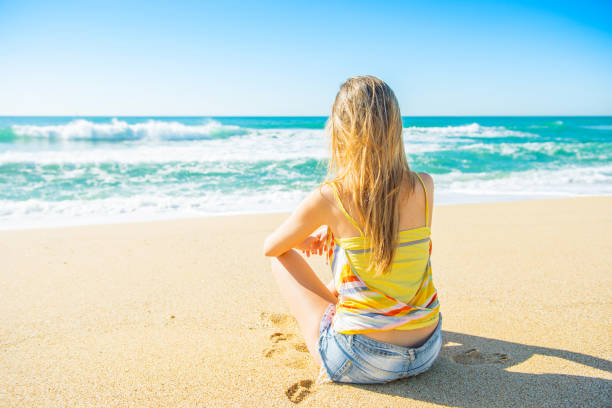 Young beautiful and blond girl sitting and relaxing on the beach stock photo