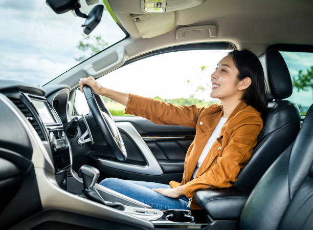 Young beautiful asian women getting new car. she very happy and excited. Smiling female driving vehicle on the road on a bright day. stock photo