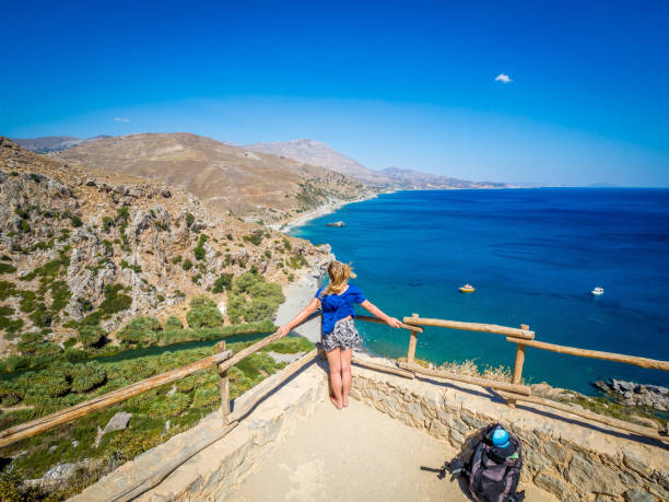 Young beautiful blonde girl contemplates and admires from a high point Preveli Beach (Palm Beach), Crete (Greece) stock photo